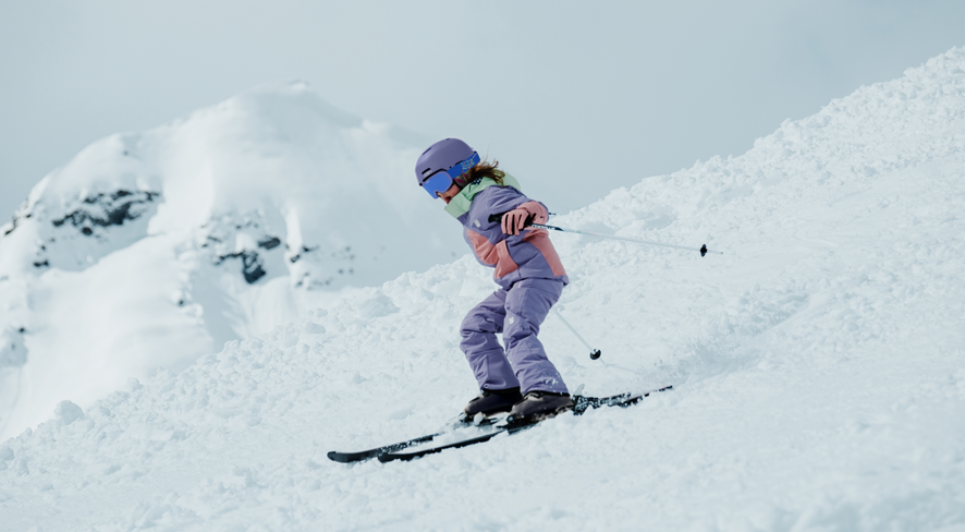 Mädchen fährt Ski in der neuen Skijacke und Skihose von der Kinderkleidermarke namuk