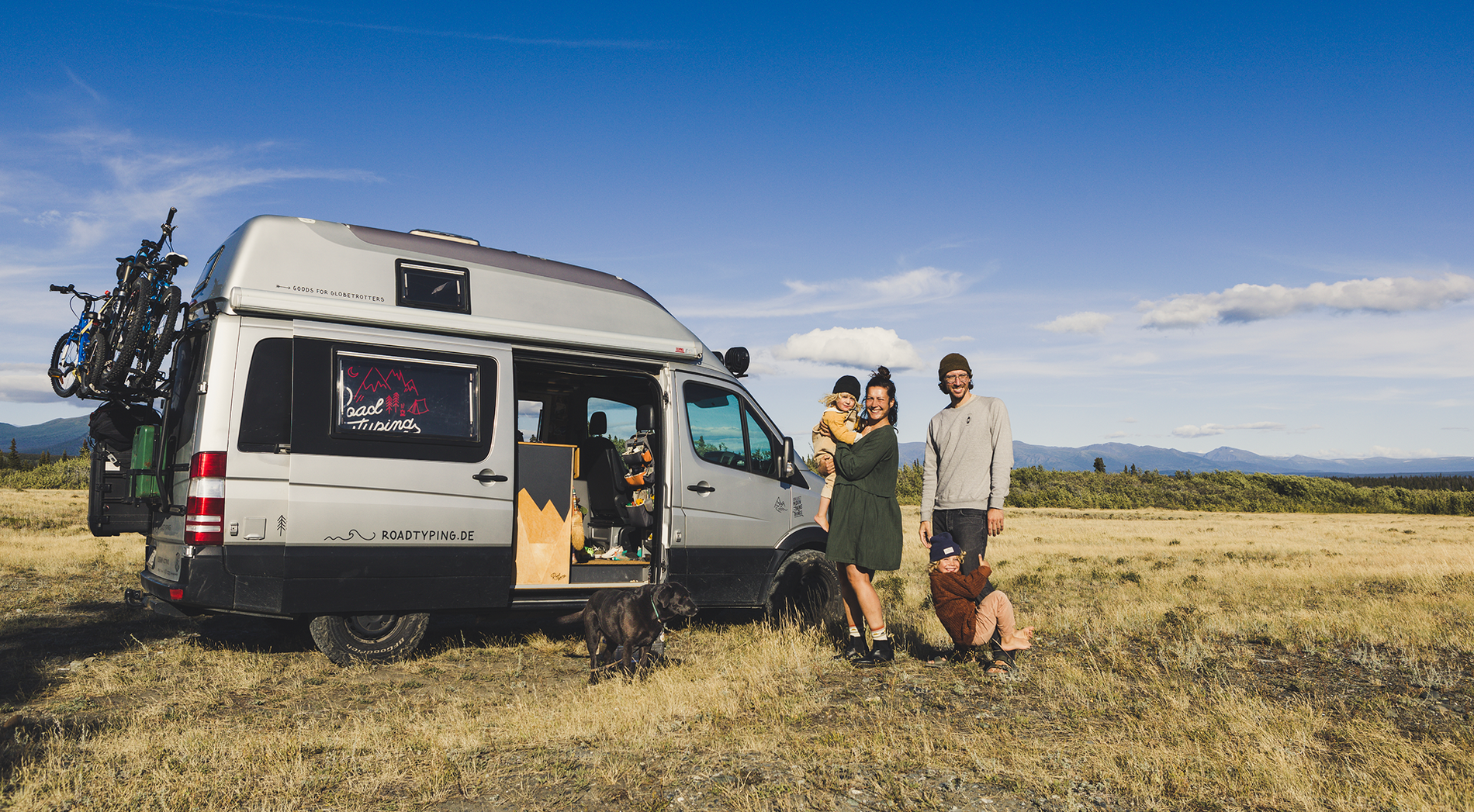 Familie von roadtyping stehen gemeinsam mit ihrem Hund vor ihrem Camper mitten in der Natur