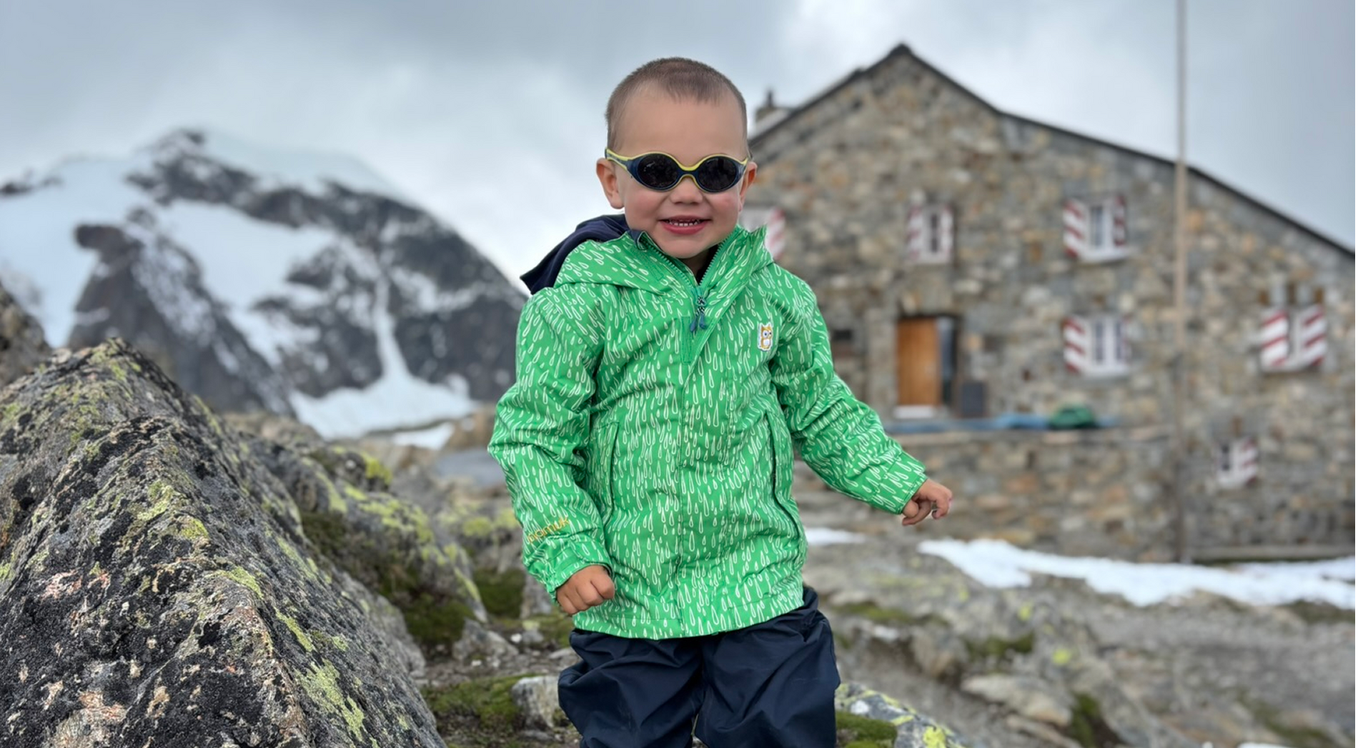 Kleiner Junge in namuk-Kleidung läuft lachend auf die Kamera zu, im Hintergrund die Tierberglihütte