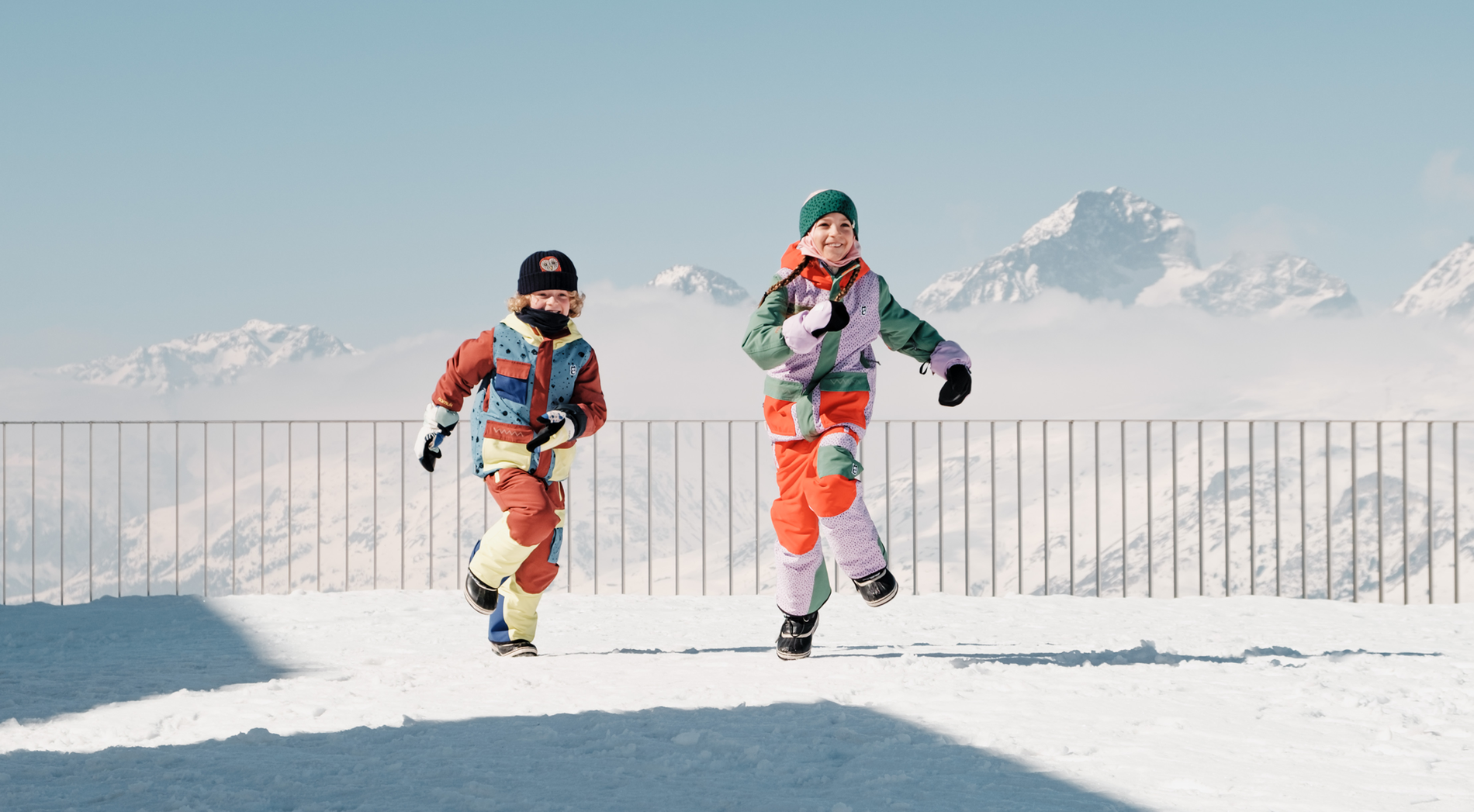 namuk Studie -  Schweizer Kinder und Outdoor-Zeit - Zwei Kinder rennen durch den Schnee vor einer Bergkulisse