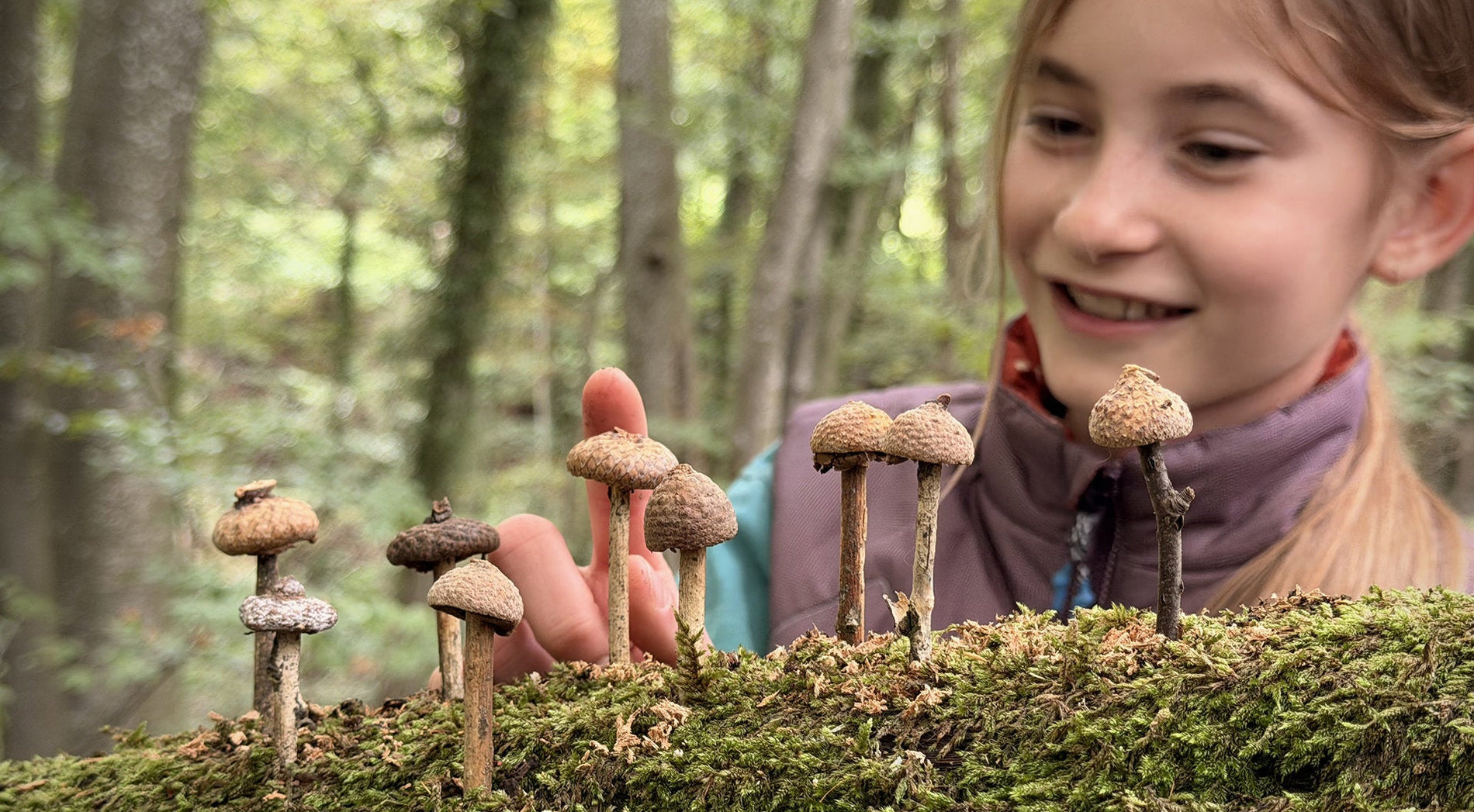 Mädchen zeigt auf gebastelte Pilze im Wald